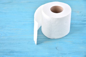 A roll of soft white toilet paper with selective focus on textured wooden background. Restroom concept with toilet paper on blue wood backdrop. Daily hygiene cleanser. Recycling toilet paper. 