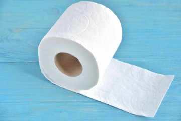 A roll of soft white toilet paper with selective focus on textured wooden background. Restroom concept with toilet paper on blue wood backdrop. Daily hygiene cleanser. Recycling toilet paper. 