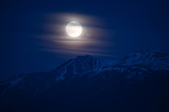 Moon rising behind the peak of snow covered mountain