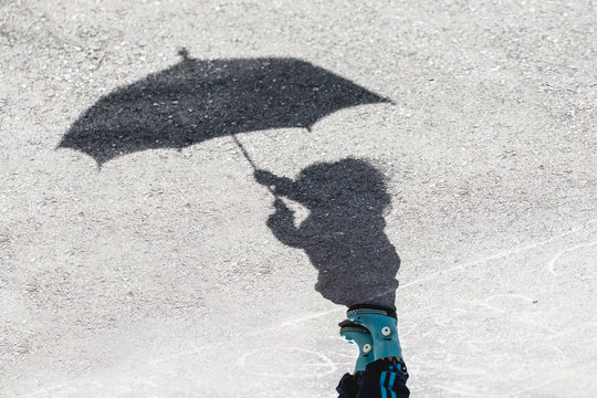 Shadow portrait of a little girl in blue rubber boots holding up an umbrella