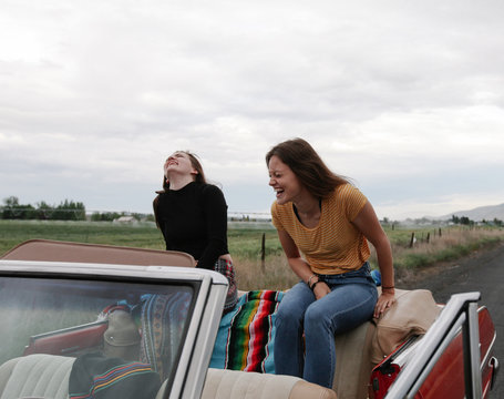 teens stopped on side of road sit on backseat laughing