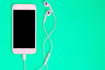 White smartphone on the green background with headphones. View from above.