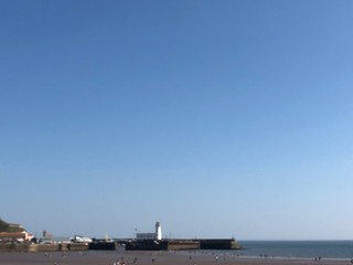 Fototapeta na wymiar Looking across beach at low tide towards the harbour lighthouse in Scarborough, UK on a bright blue sky sunny day