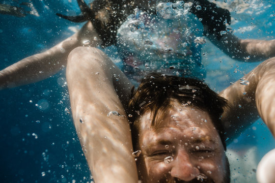 Father and daughter play together underwater in a swimming pool during a hot summers day
