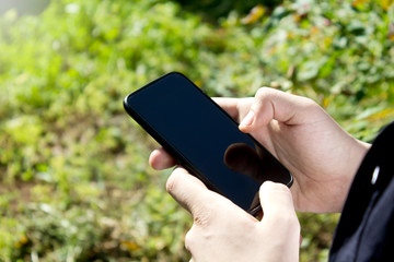 Male hands holding mobile phone in garden background.