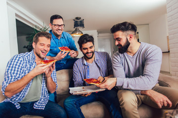 Group of four male friends eating pizza at home.