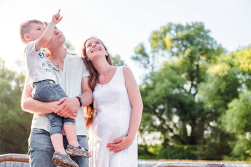 pregnant woman, her husband and son together for a walk in the park. Look somewhere up