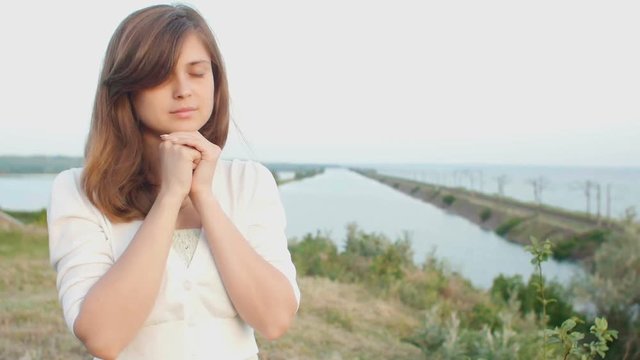 young beautiful woman turning to God in nature, the girl praying folded her hands at the chin, concept of religion
