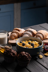 Muffin, croissant and bowl corn flakes. Sweet food. Healthy delicious meal. Black background. Kitchen.