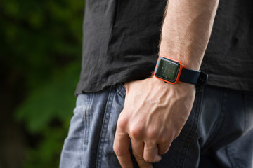 Smart watch close up photo. Man posing in summer park. Body detail on man’s hand in the jeans pants pocket.