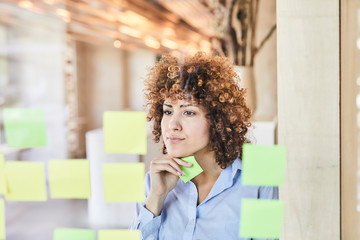 businesswoman brainstorming with post-its on glass pane