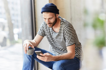 Young man holding coffee cup using cell phone