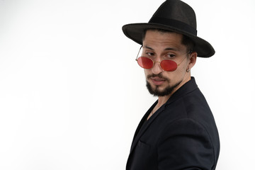 Stylish bearded young man in black trendy suit and hat in red sunglasses, looking down right isolated over white background, copyspace for your text