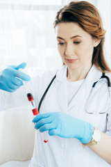 doctor in latex gloves holding syringe with blood sample and test tube
