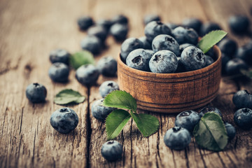 Freshly picked blueberries in wooden bowl on wooden background. Healthy eating and nutrition.