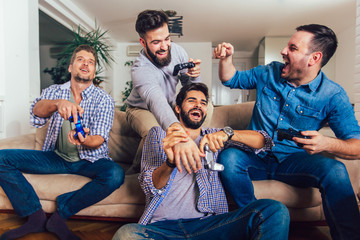 Smiling male friends playing video games at home and having fun.