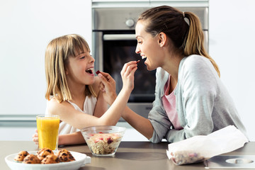 Obraz na płótnie Canvas Beautiful mother and daughter feeding cereals to each other at home.