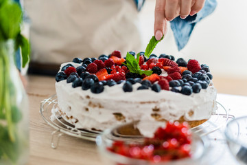 Young woman preparing a cream cake with fresh fruits