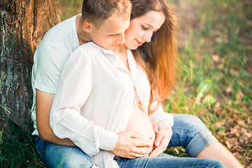 pregnant woman and her husband are sitting on the grass