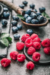 Fresh berries with raspberries, blueberries, blackberries in bowl on a stone stand on a dark metal background.