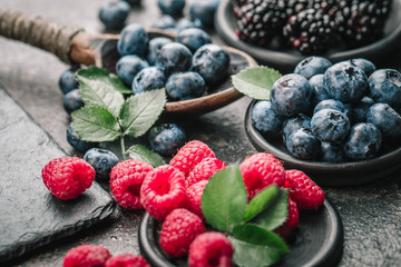 Fresh berries with raspberries, blueberries, blackberries in bowl on a stone stand on a dark metal background.