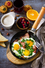 Breakfast scrambled eggs with bacon, coffee, berries, cookies, nuts and juice on dark table surface.