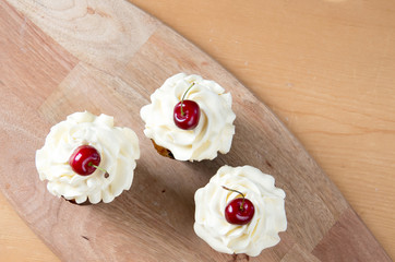 Three sweet cupcakes with creme and cherry top view