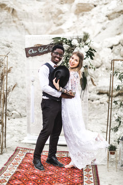 Funny hippy Wedding couple dressed in boho style are staying before the wedding arch in canyon outdoors and smiling. boho wedding. boho style.