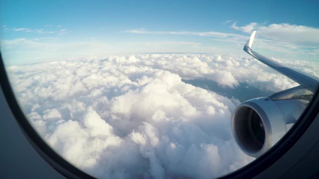 Airplane flying slightly above the clouds. Inside view through the window of an airplane of the wing and turbine. Clouds moving fast below the plane. Brazilian terrain.