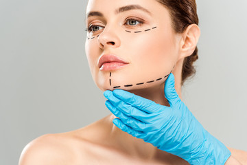cropped view of plastic surgeon touching face of attractive woman with marked face isolated on grey
