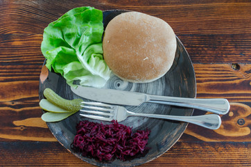 Hamburger bun and lettuce with cutlery on plate. Overhead view on table