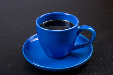 Blue cup of coffee on black wooden background.
