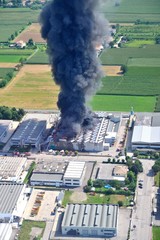 Factory fire with black smoke that causes pollution exits the building and firefighters at work