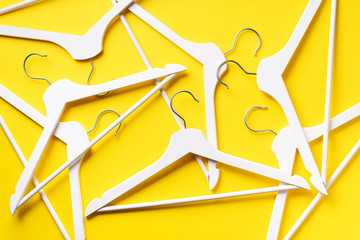White clothes hangers on yellow background with copy space. Flat lay. Top view. Minimalism style....