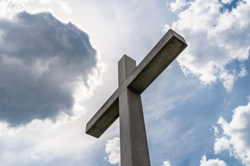A large concrete cross on a cemetery against a blue sky with white clouds.