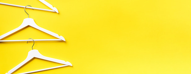 Top view of white clothes hangers on yellow background with copy space. Flat lay. Minimalism style. Creative layout. Fashion, store sale, shopping concept. Banner for feminine blog