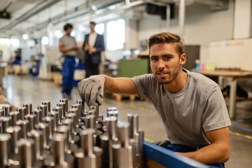 Smiling steel worker examining manufactured rod cylinders in a factory.