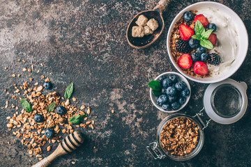 Healthy breakfast with granola, yogurt, fruits, berries on dark metal background. Summer homemade...