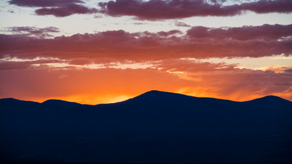 Fototapeta na wymiar Sunset silhouettes a mountain range and colors the sky and clouds in yellow, orange, purple, and pink - Jemez Mountains near Santa Fe, New Mexico