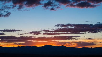 Naklejka premium Zachód słońca zarysowuje pasmo górskie i oświetla dramatyczne wieczorne niebo fioletowymi i różowymi chmurami - Góry Jemez w pobliżu Santa Fe w Nowym Meksyku