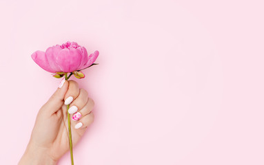 Woman hand with trendy nail art manicure holding peony flower on pink background