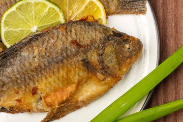 Fried fish on a white plate with lemon and lime slices. Ready meal. Close up