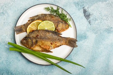 Fried Carp fish on a plate with lemon and lime slices, with greens on a blue background. Ready meal. Copy space