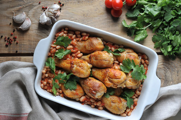 Chicken drumstick with beans and tomatoes. Garlic, spices and cloth napkin complement the composition. Wooden background. View from above. Close-up.