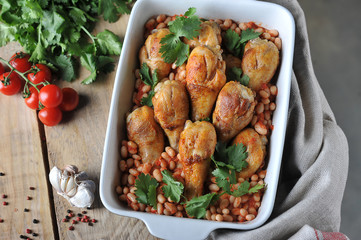 Chicken drumstick with beans and tomatoes. The concept of simple rustic food. Wooden background. View from above. Close-up.