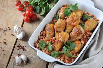 Chicken drumstick baked with beans and tomatoes. Garlic and spices complement the composition. The concept of simple rustic food. Wooden background. Close-up.