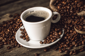 Coffee cup with coffee beans on wood background.