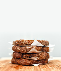 Hamburger patties stacked on wooden cutting board with empty space