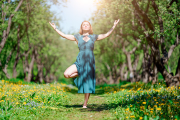 Full-length photo of girl with closed eyes in long green dress doing yoga in forest