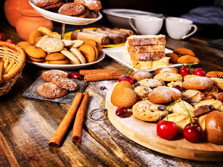Oatmeal cookies and sand chocolate cake with cherry berry and crispy wafer rolls with cream on cutting board on wooden table in rustic style. Limitations for diabetics. Cooking various dishes.